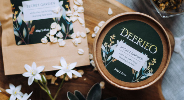 Deerieo Secret Garden natural exfoliating face mask on wooden board with white flowers.